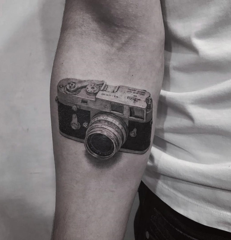 Camera tattoo located on the wrist, illustrative style.